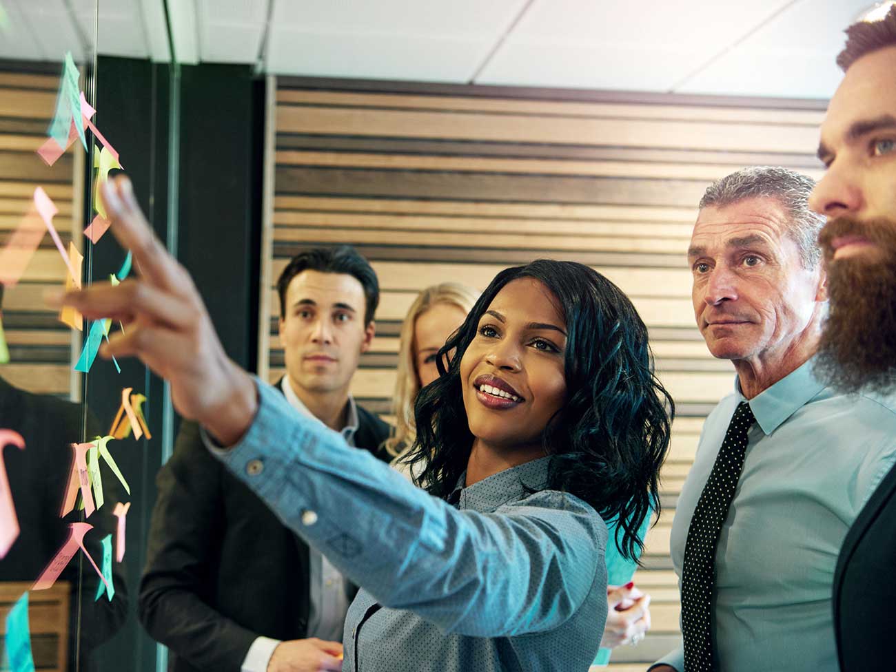 Smiling black woman pointing to a white board while surrounded by her co-workers