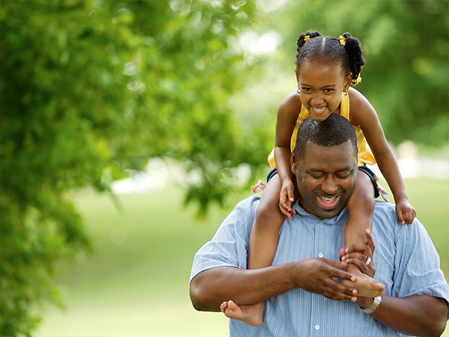 African American dad carrying daughter on his shoulders outdoors