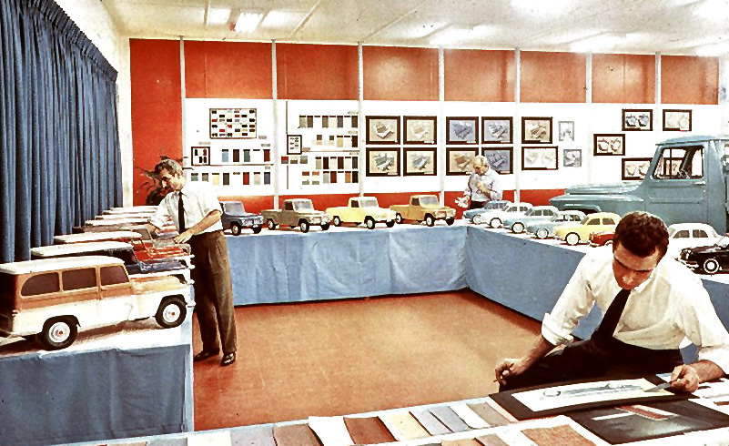 Man seated in a showroom with miniature model jeeps seated and examining an illustration