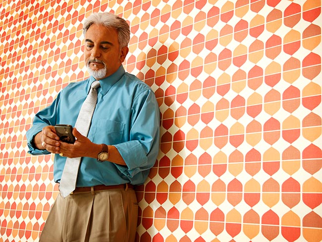 A bearded business man leaning against a wall and looking at his mobile phone.