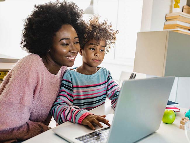 Black mother helping her daughter with school work at home on a laptop
