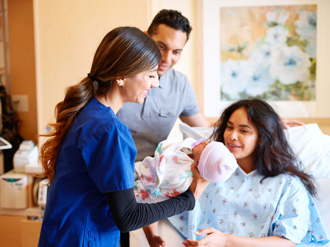 nurse handing newborn baby to mother
