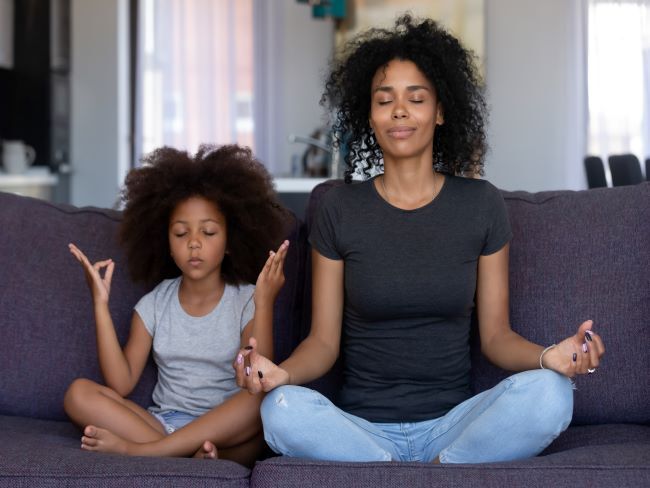 woman and young girl sitting on a sofa with their eyes closed meditating