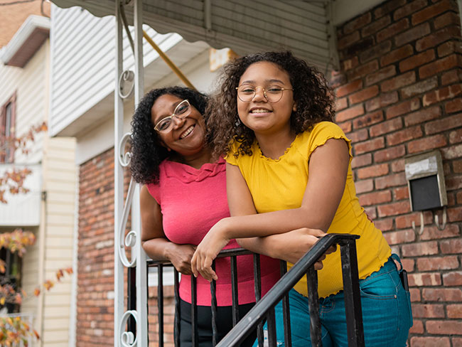 A happy mother and daughter stand on their front porch