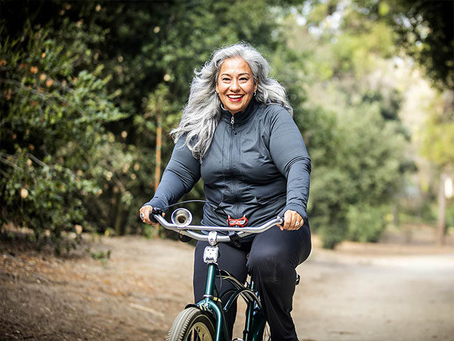 Senior Mexican woman smiling as she's riding a bicycle.