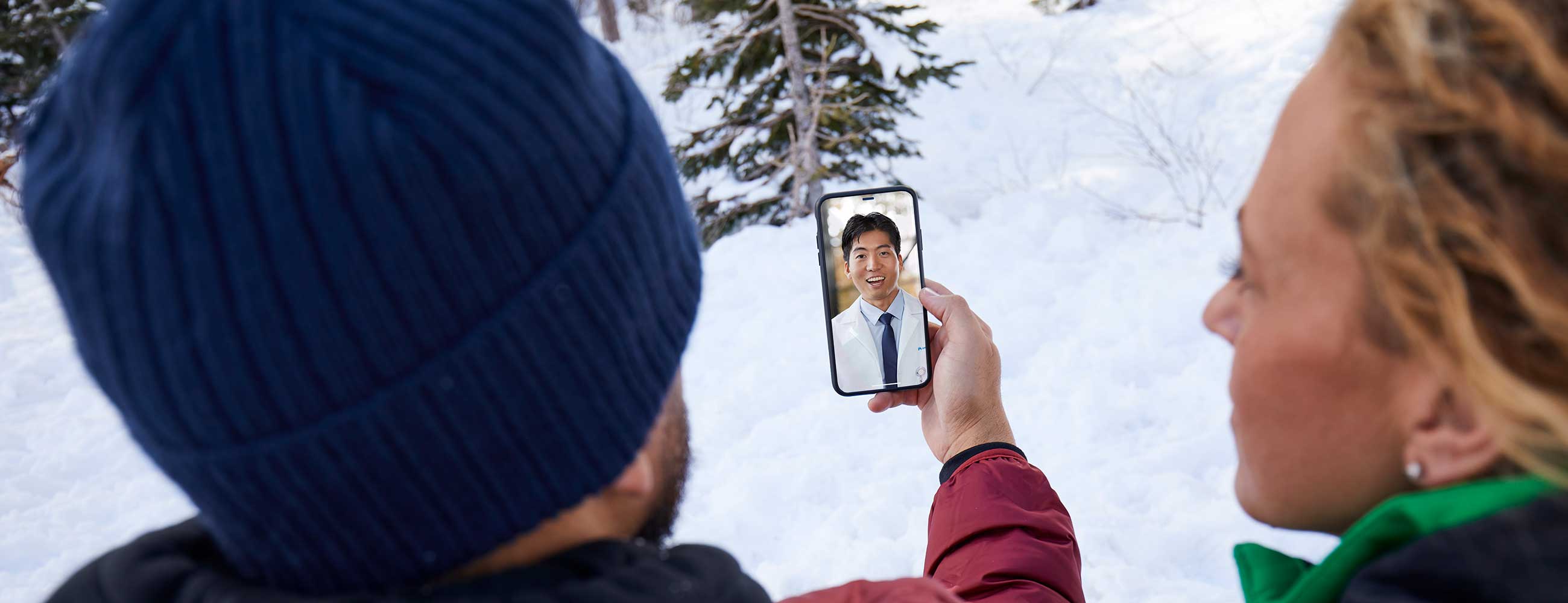 A man and woman in a telehealth visit with a physician while outdoors, in the snow.