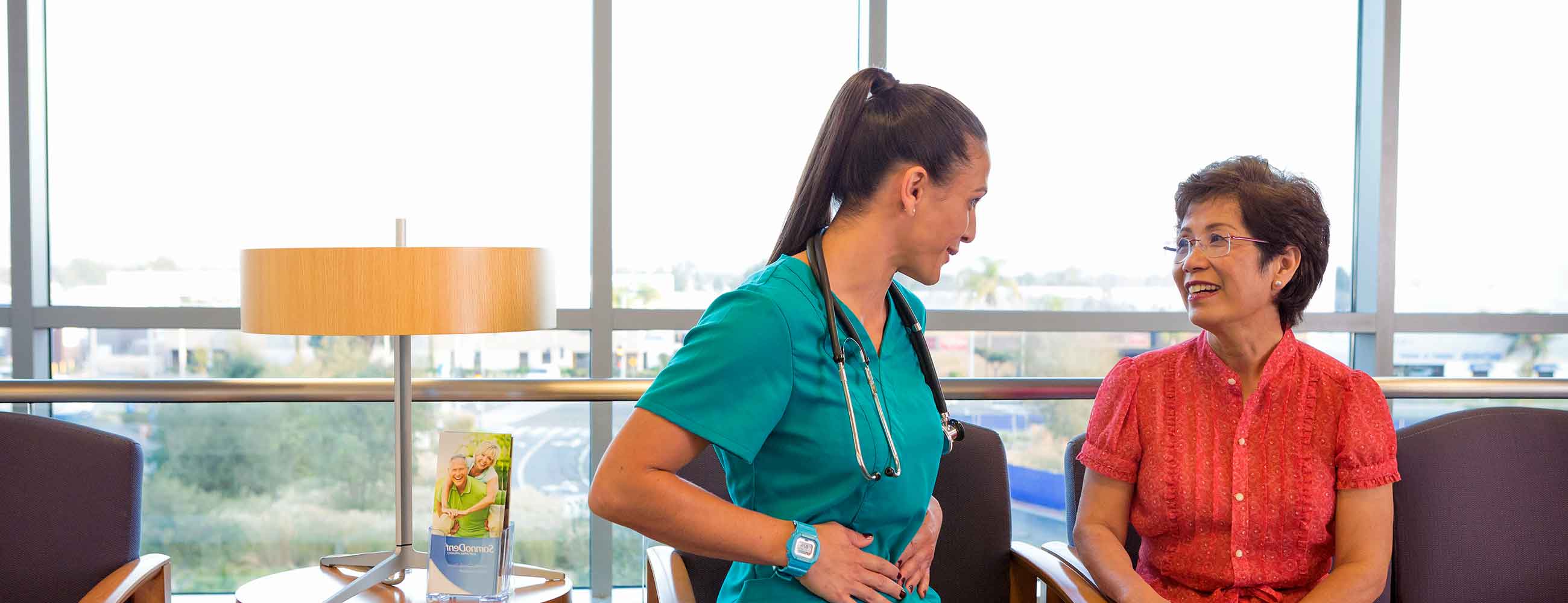 A female physical therapist in green scrubs, consulting with her senior female patient. 