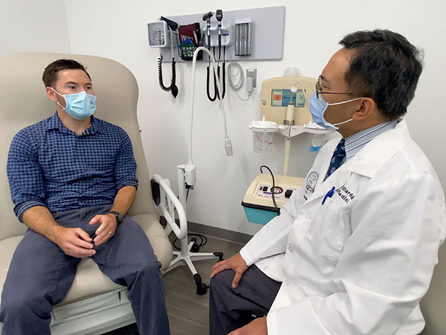Patient in exam room with physician, both wearing facemasks.
