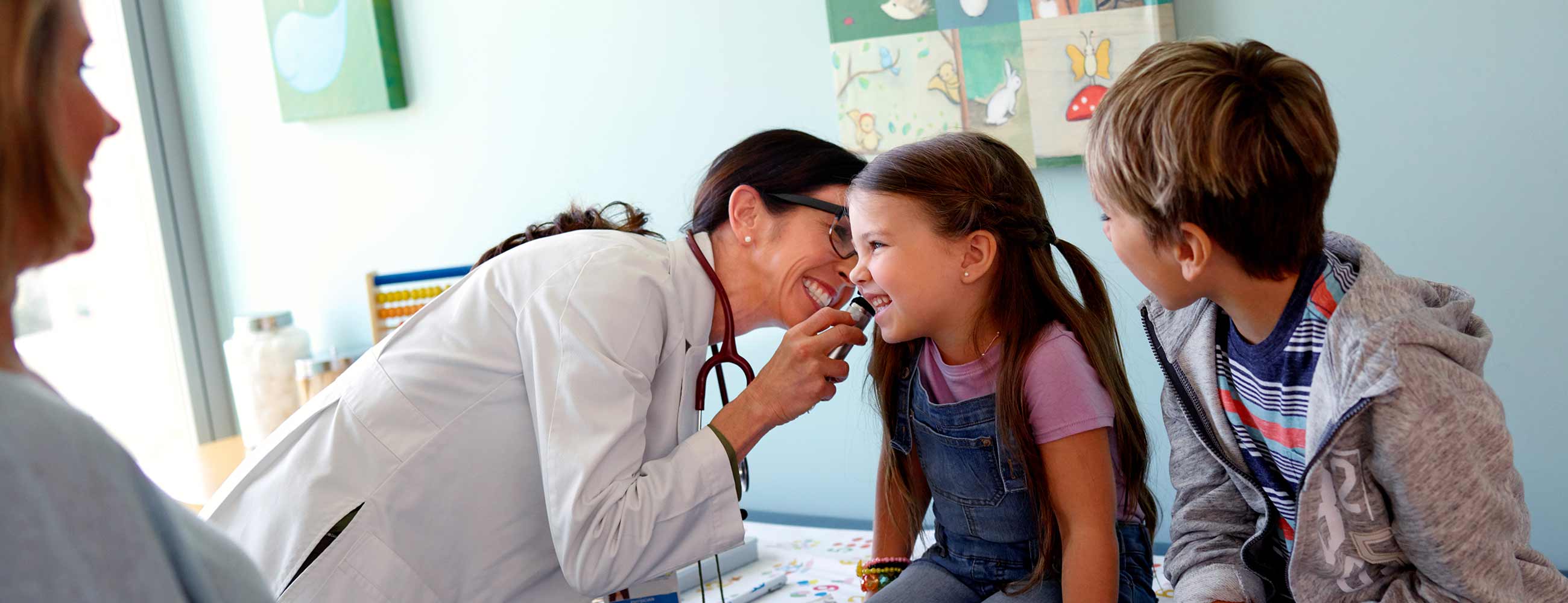 A smiling physician examining a young girl's ear with an  otoscope.