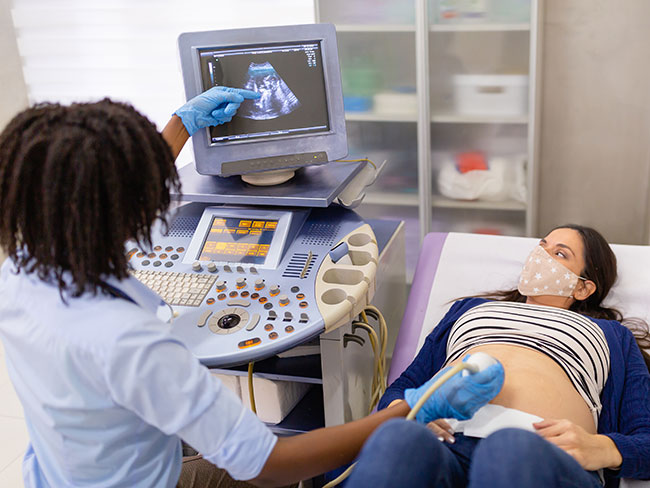 Female doctor doing ultrasound examination of a pregnant woman wearing a facemask.