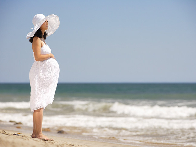 Pregnant woman standing on a beach gazing at the ocean