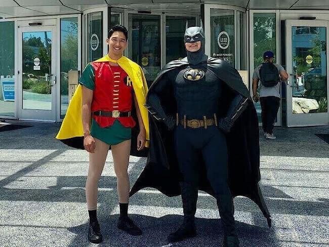 2 men dressed in Batman and Robin costumes standing outside a Kaiser Permanente building