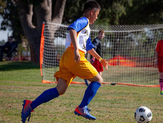 An athlete kicks a soccer ball down a field toward a soccer goal.