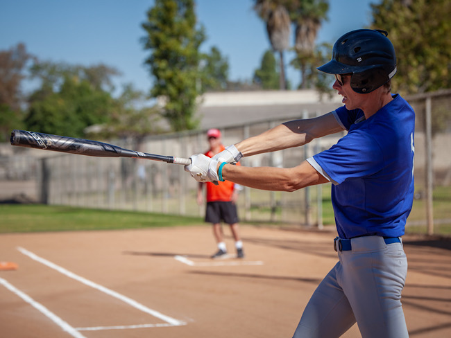 Parker White, wearing a blue jersey and softball helmet, swings a bat.