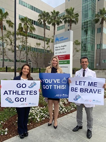 Three individuals holding signs with messages of encouragement in front of a medical facility. 