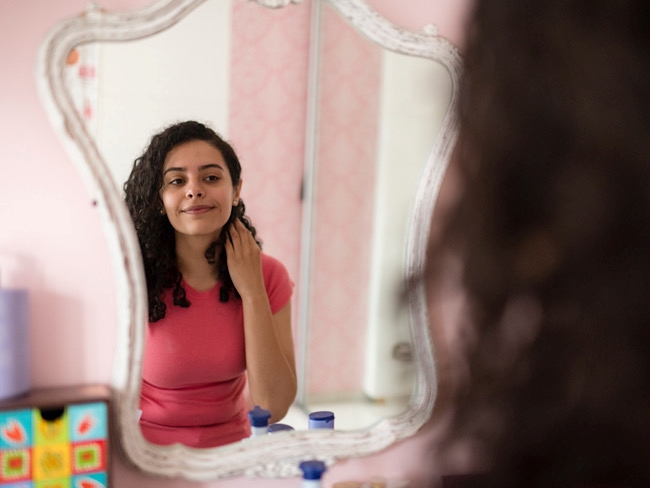 A teenage girl adjusts her hair while looking into a mirror.