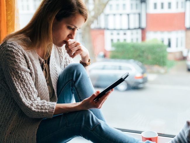 Woman sitting near window looks anxiously at her phone.