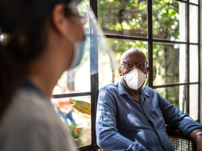 Senior man wearing a face mask, talking with his doctor.