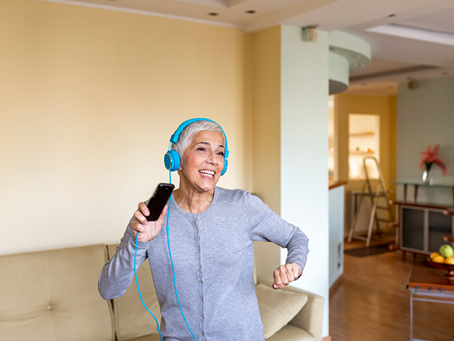 senior woman wearing headphones dancing alone in her living room
