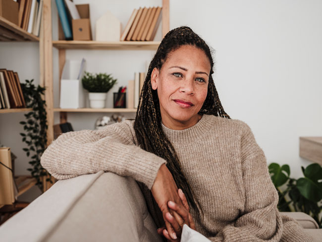 Black woman in braids sitting on a couch, looking into the camera with a serious expression 