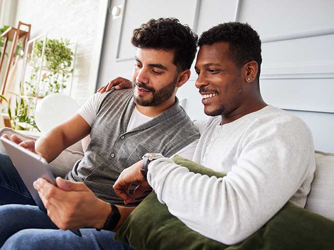 Smiling young multiracial gay couple using a tablet computer while sitting together 