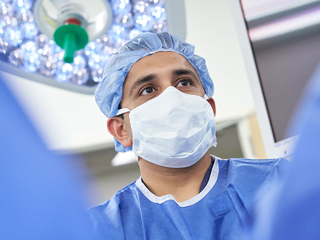 A male surgeon in scrubs and face mask in surgery room.