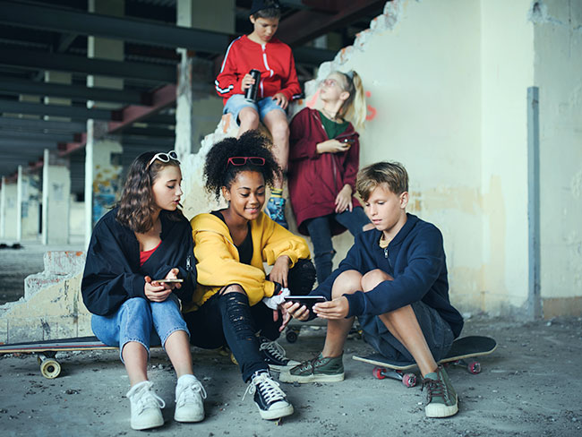 Group of teenagers hanging out in an abandoned building, using smartphones.