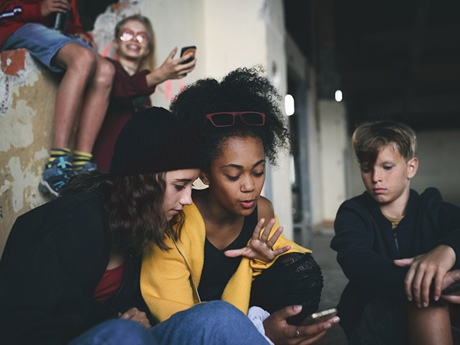 Group of teenagers sitting indoors in abandoned building using smartphones