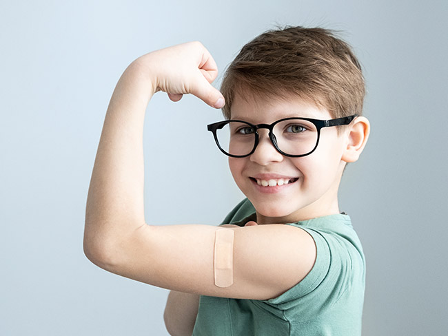 Young boy smiling and holding up arm with bandage from his vaccination.