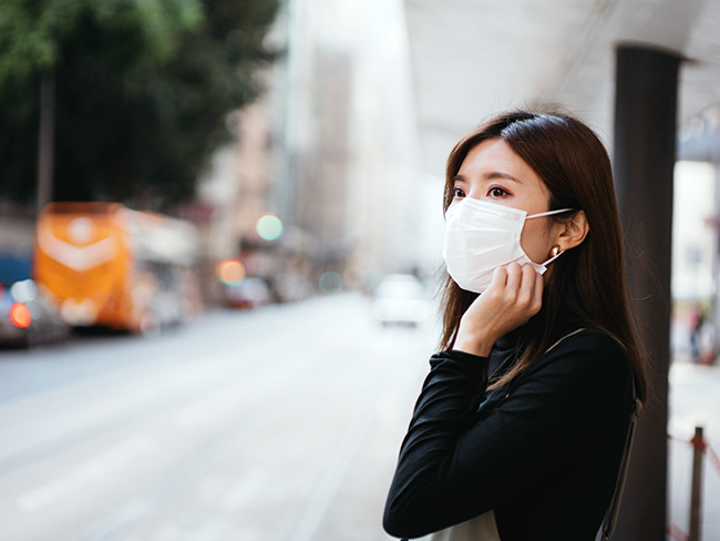Young Asian woman wearing a protective face mask while waiting for public transportation.