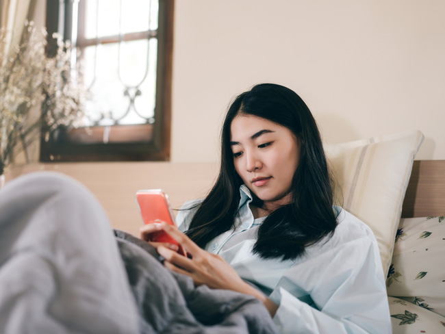 young woman wearing pajamas in bedroom looking at smartphone