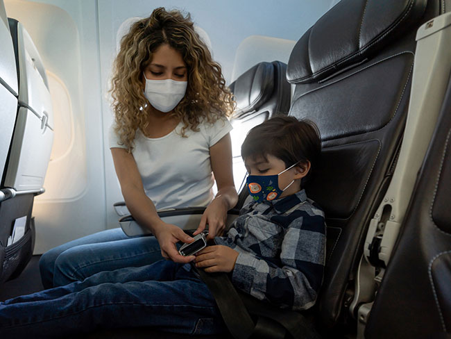 woman inside airplane helping young boy with seatbelt