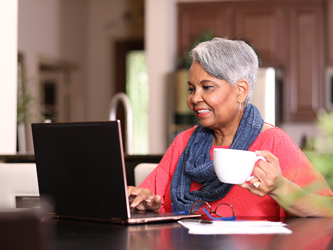 Senior adult woman at home sitting at kitchen table using laptop computer.