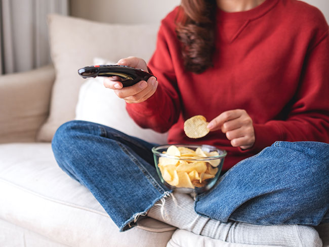 Woman eating chips and holding remote control while sitting on the couch