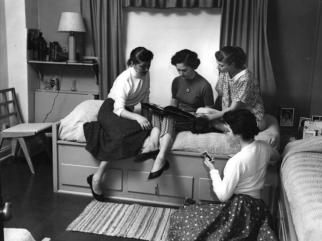 4 young women inside a dorm room reading a book