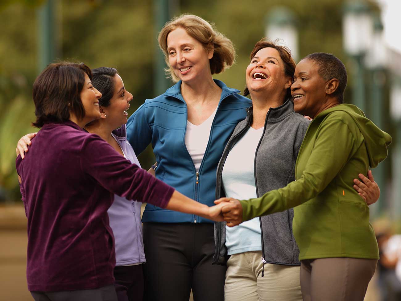 Group of 5 laughing women, standing in a circle with hands joined