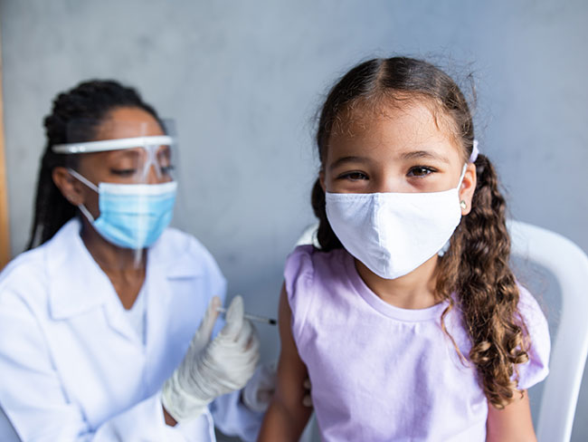 A young girl in a face mask smiling while getting a vaccine.