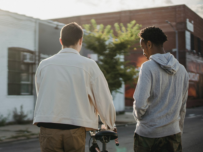 Shot from behind of two young men pushing a bicycle down a city street.