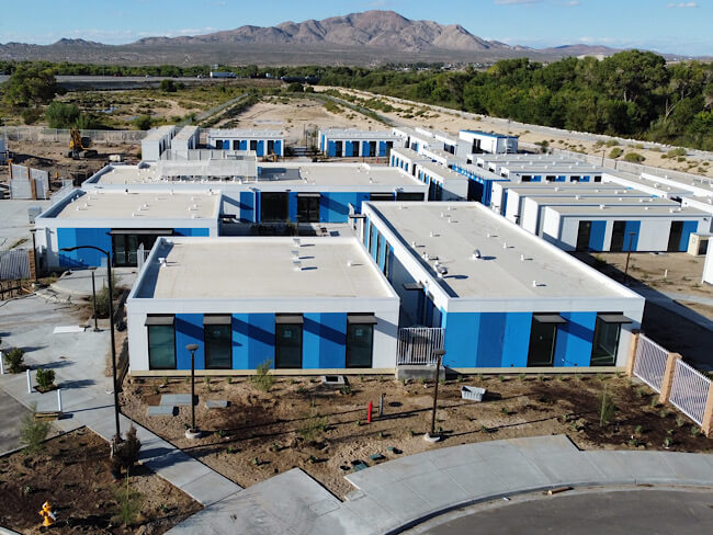 An aerial view of the Victorville Wellness Center, a modular building complex with blue and white striped walls in a desert setting with mountains.