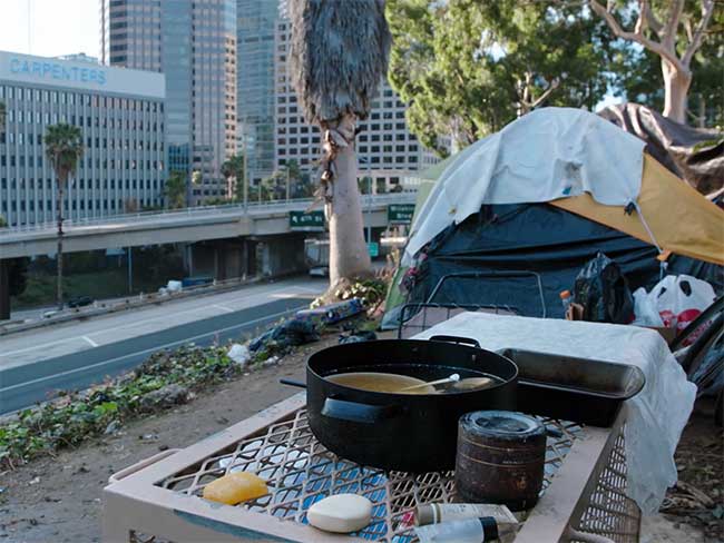 A tent, with a pot of soup in front, next to a freeway overpass.