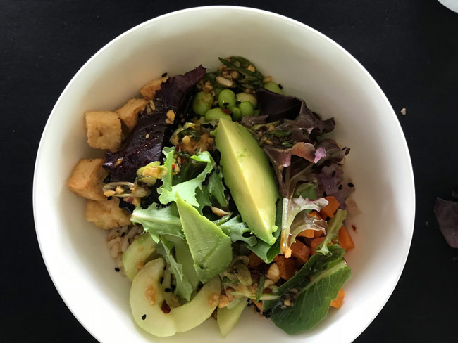 Overhead picture of grain bowl that includes rice, greens, avocado, and tomatoes