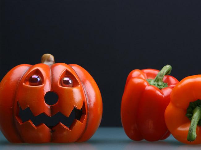Decorative jack-o'-lantern on left, with two whole red-orange bell peppers on right.