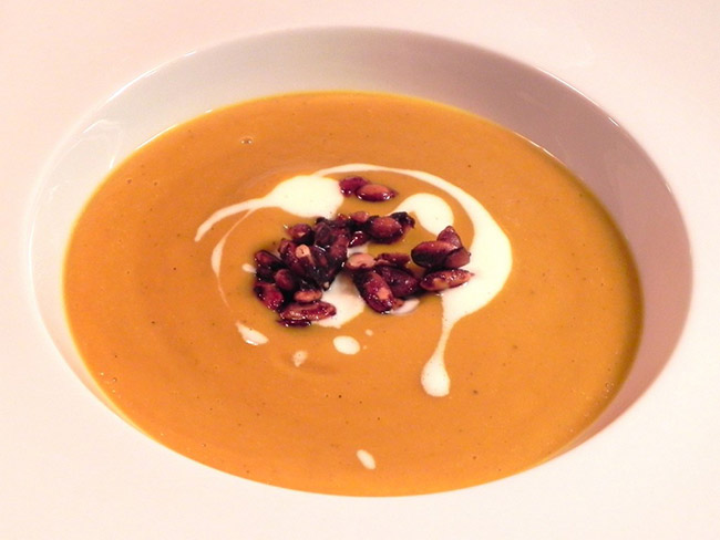 Top down view of a bowl of kabocha squash and fennel soup topped with a swirl of sour cream and pomegranate seeds.
