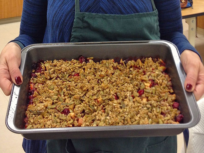 Apple cranberry crisp in a metal baking pan, held by person in an apron