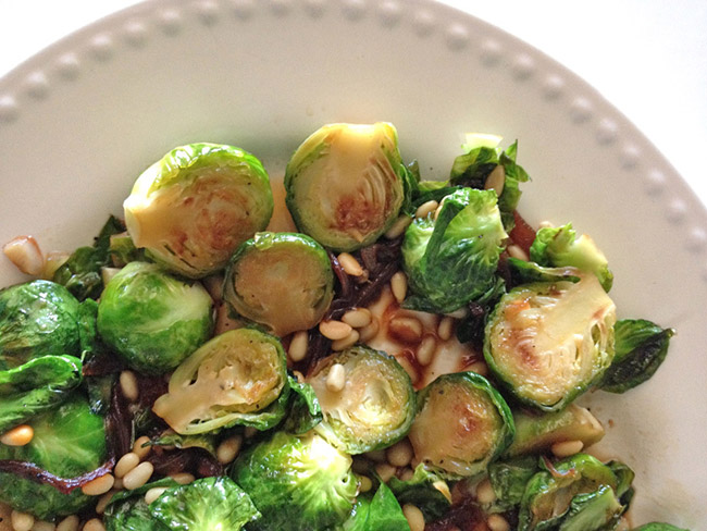 Brussels sprouts halves with pine nuts and onions on a white platter.