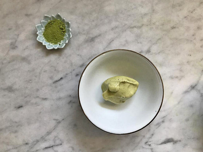 A small bowl of green frozen dessert on a marble counter.
