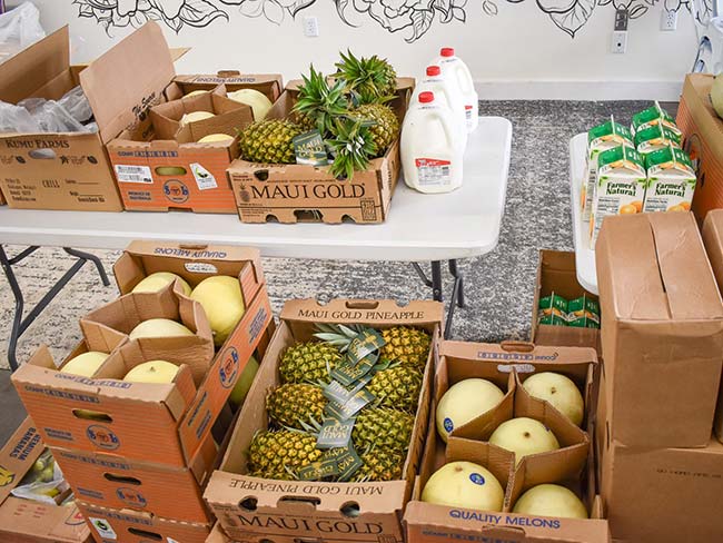 Boxes of fresh fruit stacked on a table gallons of milk and orange juice.