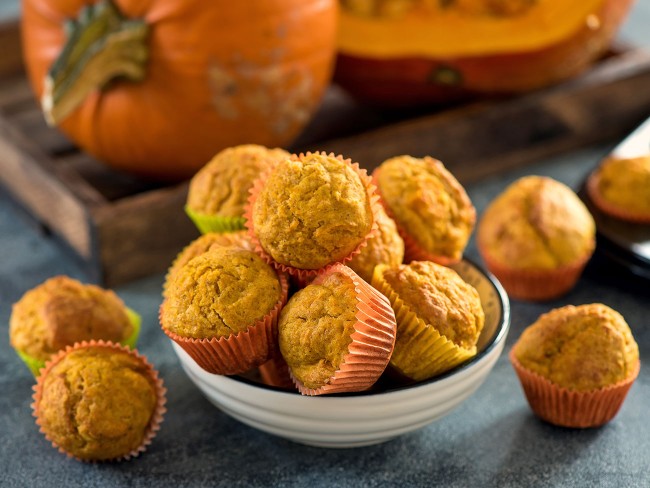 Freshly baked mini pumpkin muffins with pumpkins in the background.