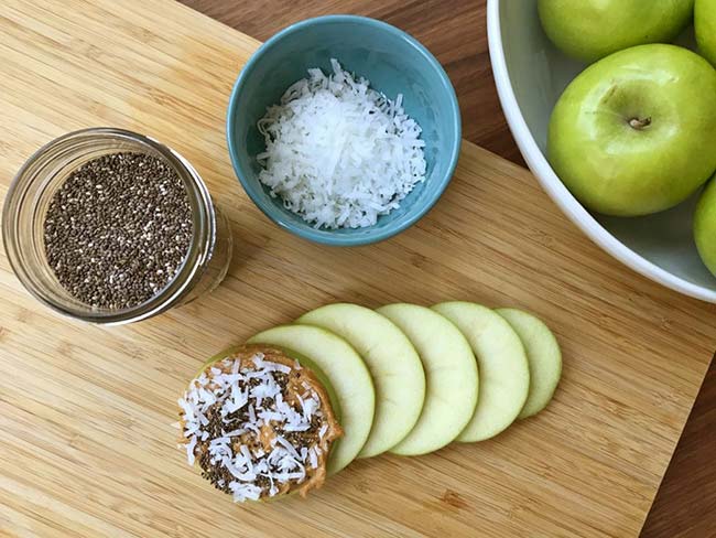 Arrangement of apple slices, one of which is topped with peanut butter, shredded coconut, and flax seeds