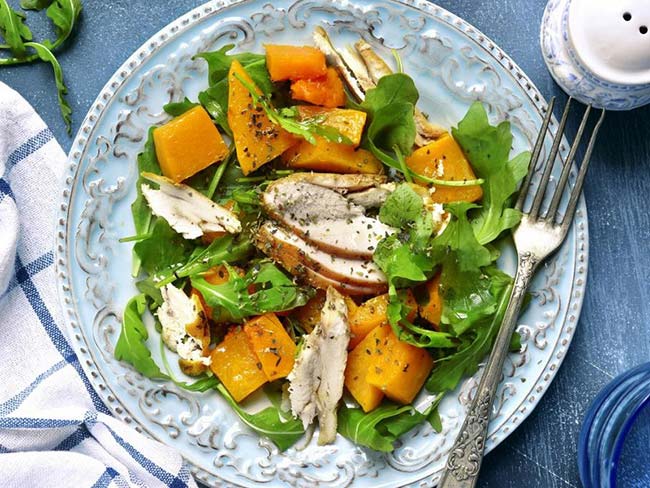 A bowl of a healthy green salad topped with turkey and pumpkin on a blue vintage plate.